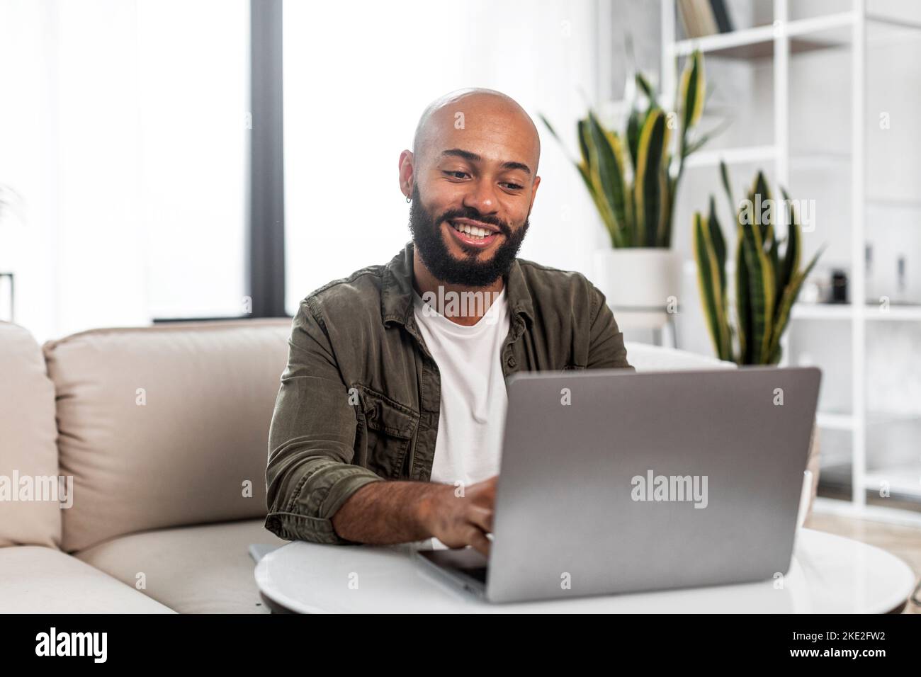 Concetto di home Office. Uomo felice e maturo che lavora su un PC portatile, seduto su un comodo divano a casa e sorridente, spazio libero Foto Stock