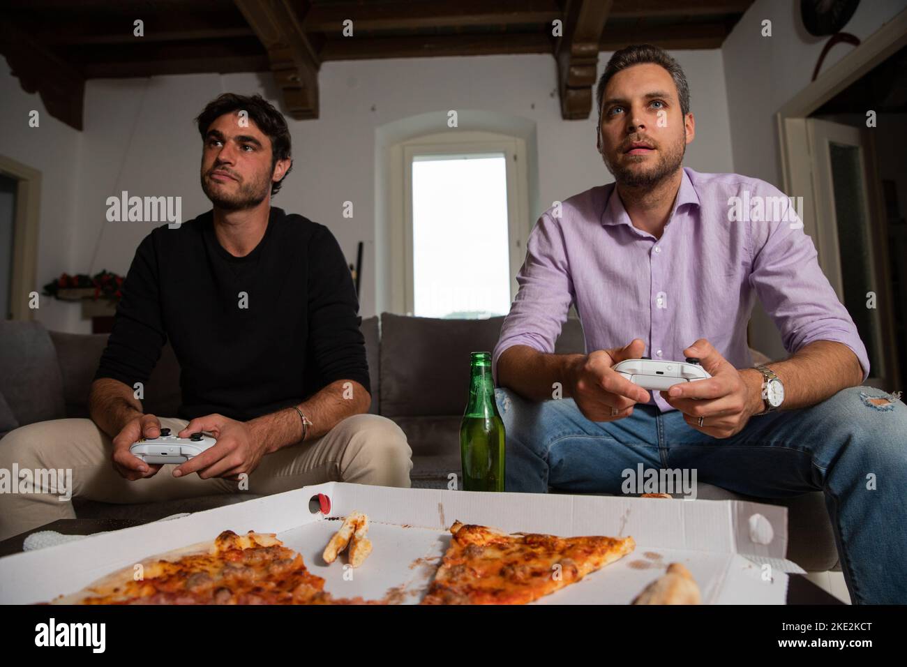 Due giovani amici felici che giocano ai videogiochi seduti sul divano. Foto Stock