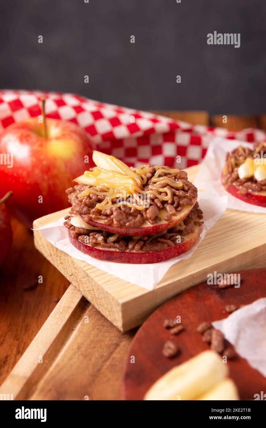 Festa creativa snack per le vacanze. Le mele si arrotolano con burro di arachidi, caramello e cioccolato farcitura di riso soffiato con fette di banana. Appetiz divertente Foto Stock