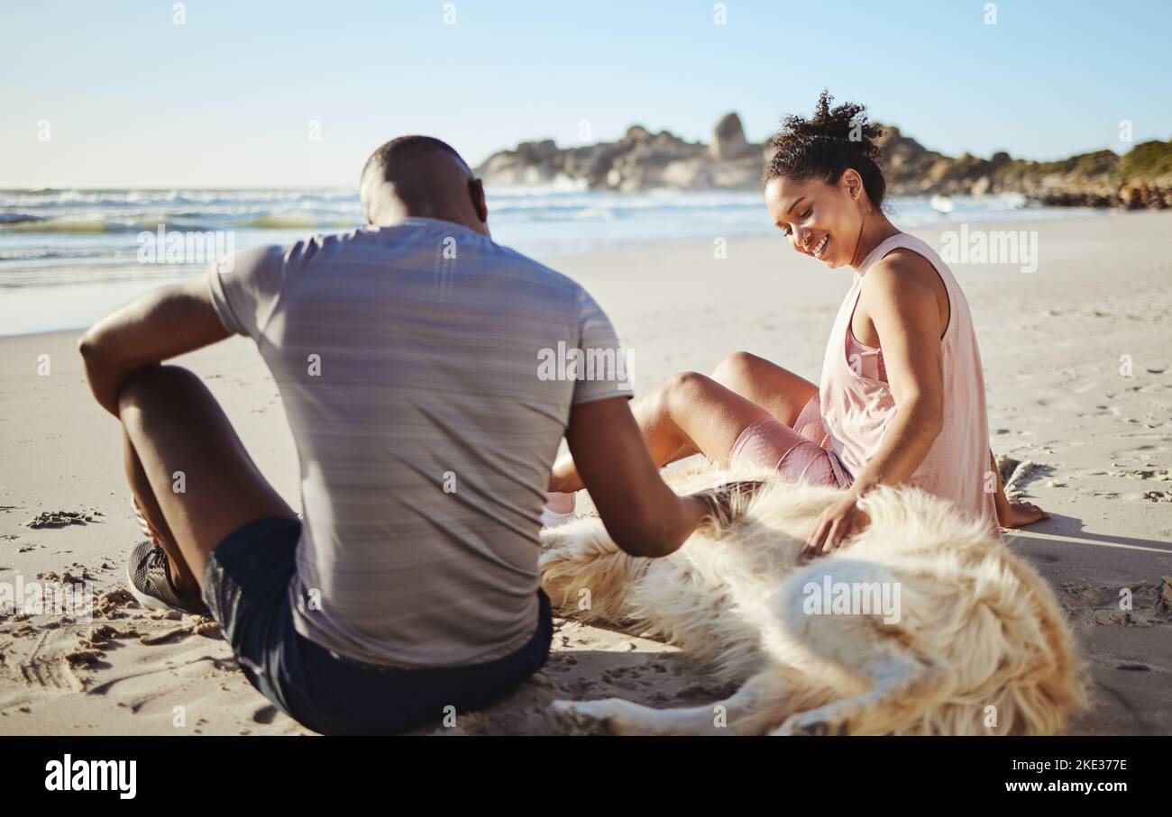 Fitness coppia rilassarsi con il cane in spiaggia, sabbia e oceano dopo l'allenamento estivo, tempo libero e divertimento al sole insieme. Felice uomo, donna e gente Foto Stock