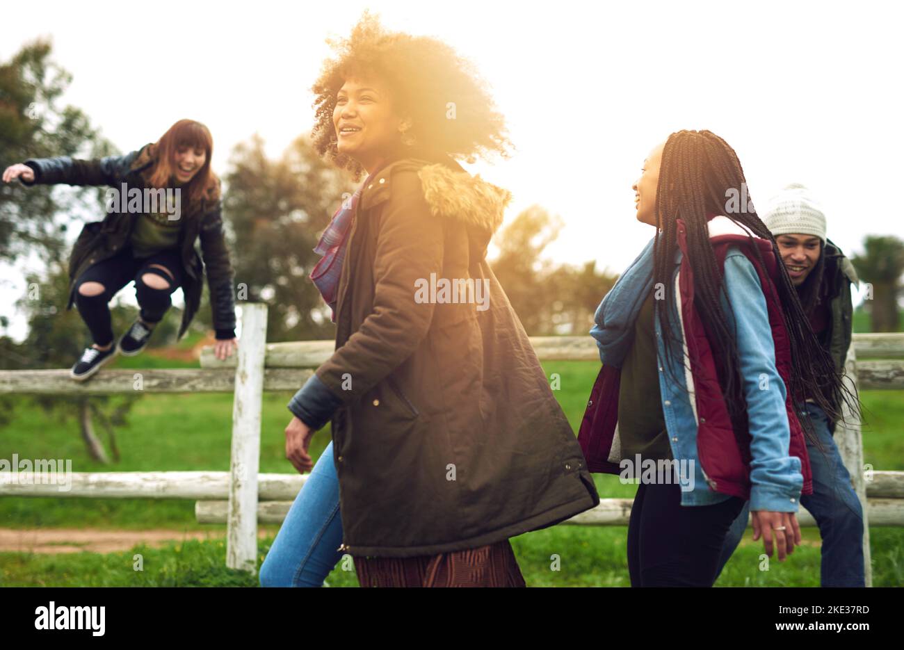 Portiamo il divertimento a tutto che facciamo. Un gruppo di amici che saltano sopra una recinzione in un campo per divertimento. Foto Stock