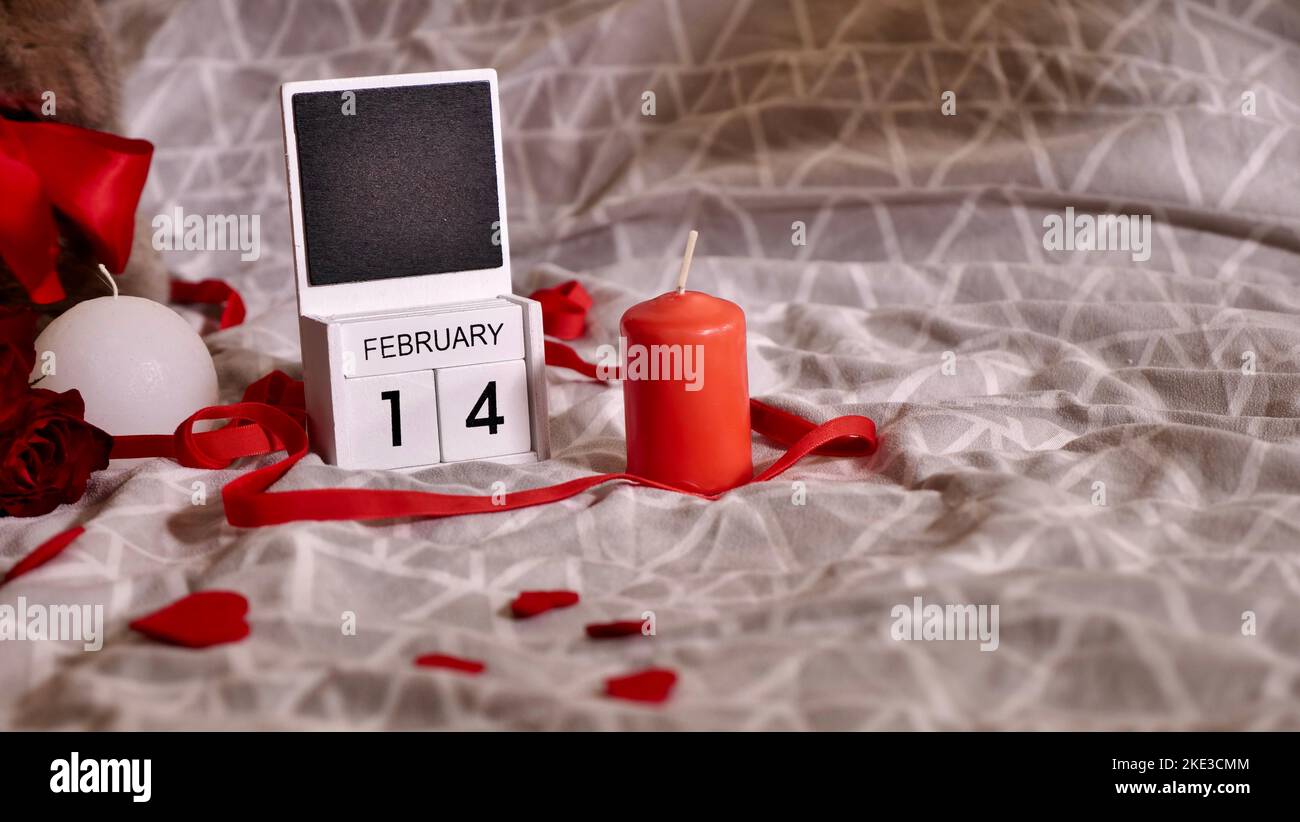 Flatlay festivo, composizione per San Valentino il 14 febbraio. Caffè in una tazza rossa, fiori di rosa rossa e calendario a casa a letto in data spaziale Foto Stock