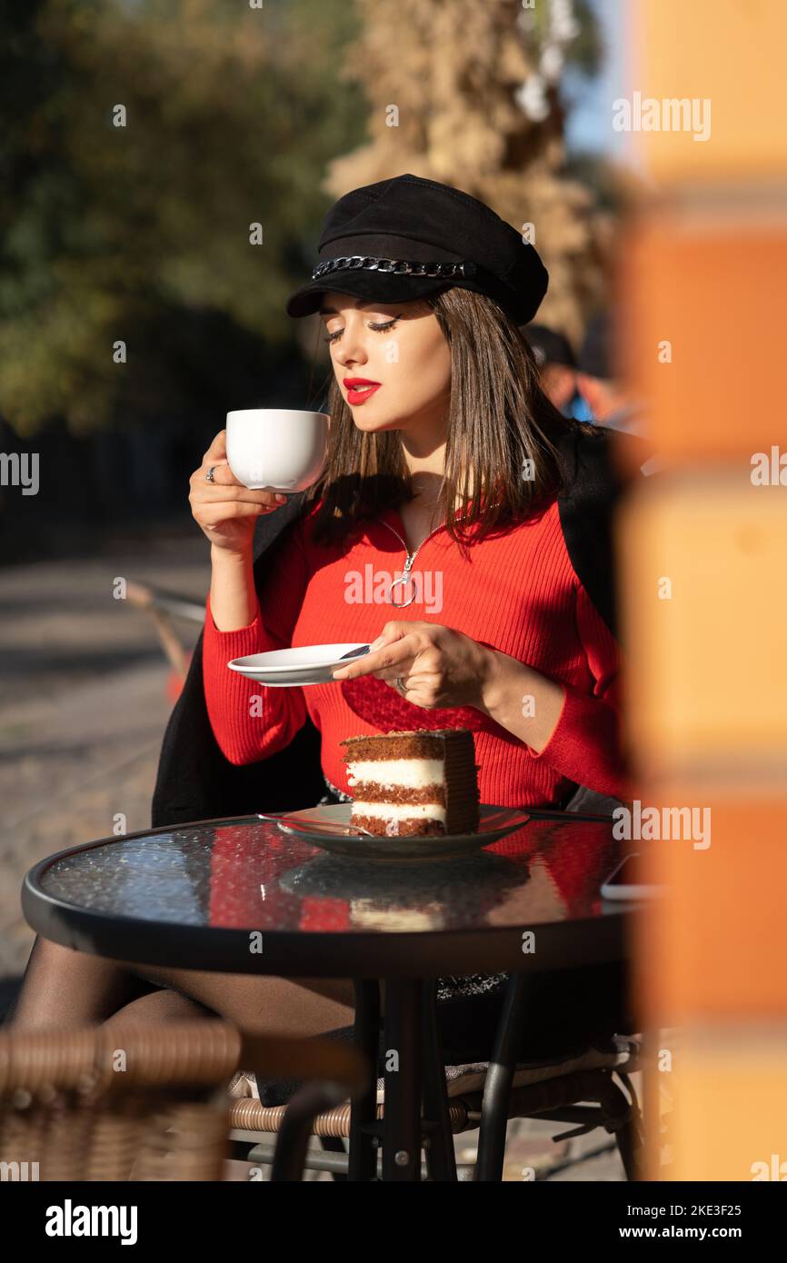 Ritratto di un'elegante donna d'affari con labbra rosse seduto in un caffè all'aperto bere caffè godendo il sole e rilassante Foto Stock