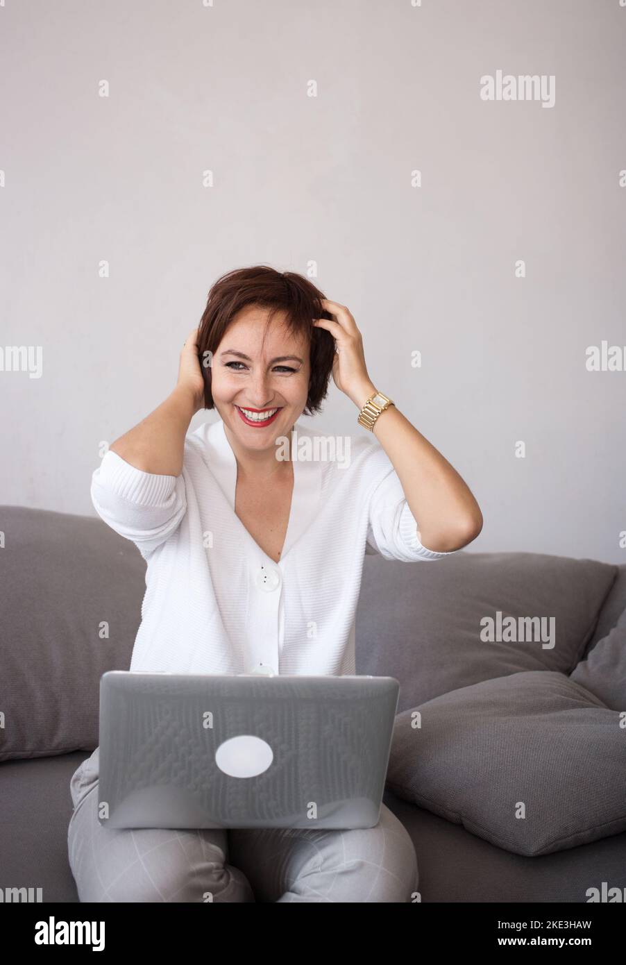 Adorabile successo felice sicuro bruna donna 35-40 anni si siede sul divano e funziona con un computer portatile. Le moderne tecnologie della comunicazione, l Foto Stock