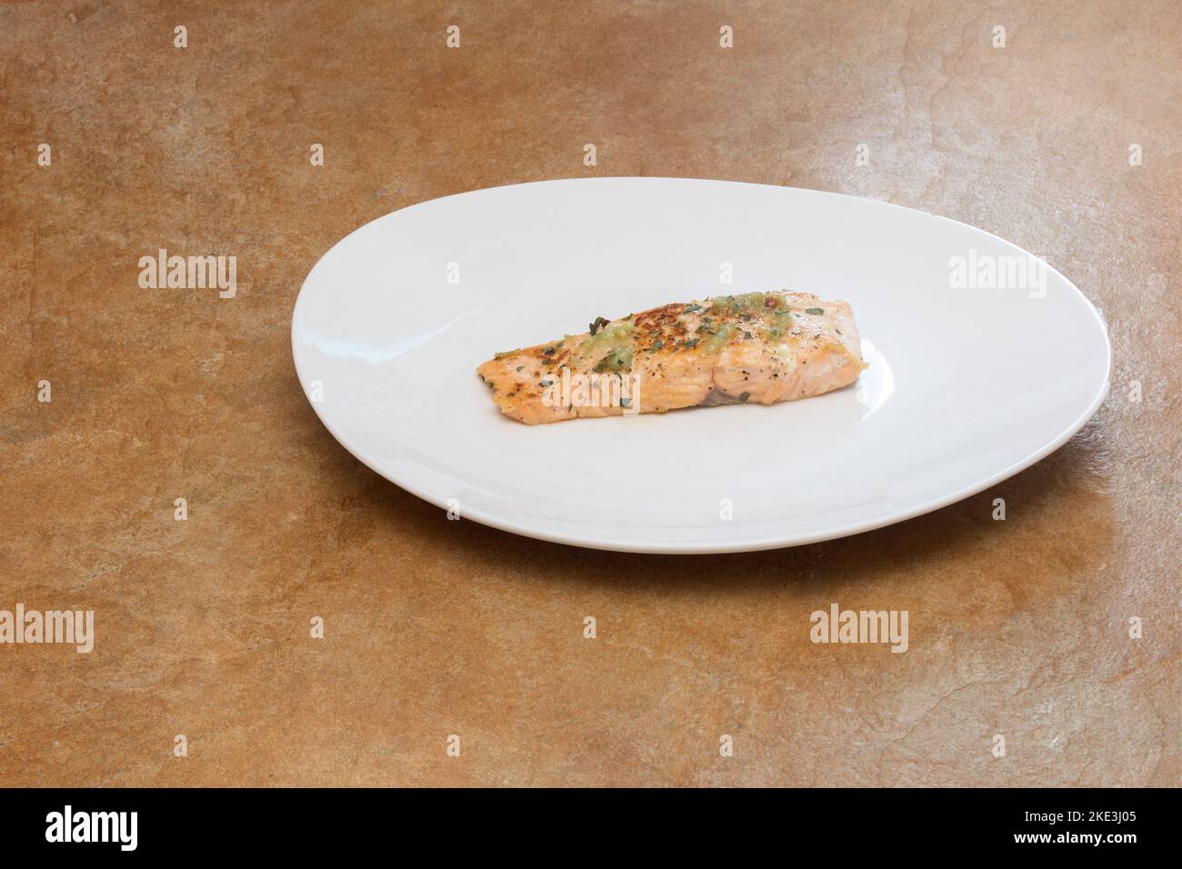 Una porzione di lombo di salmone isolato al limone con prezzemolo e aglio servito su un piatto bianco su un banco da cucina rustico. Pesce e una dieta sana. Foto Stock