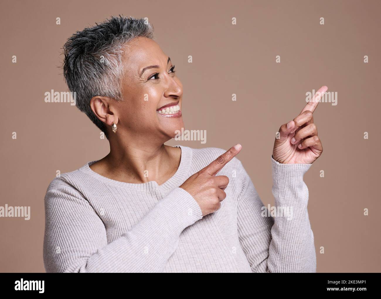 Donna matura che indica lo spazio sullo sfondo dello studio per l'introduzione sul mercato, la pubblicità o la presentazione delle idee, la scelta e la revisione. Donna felice che mostra marrone Foto Stock