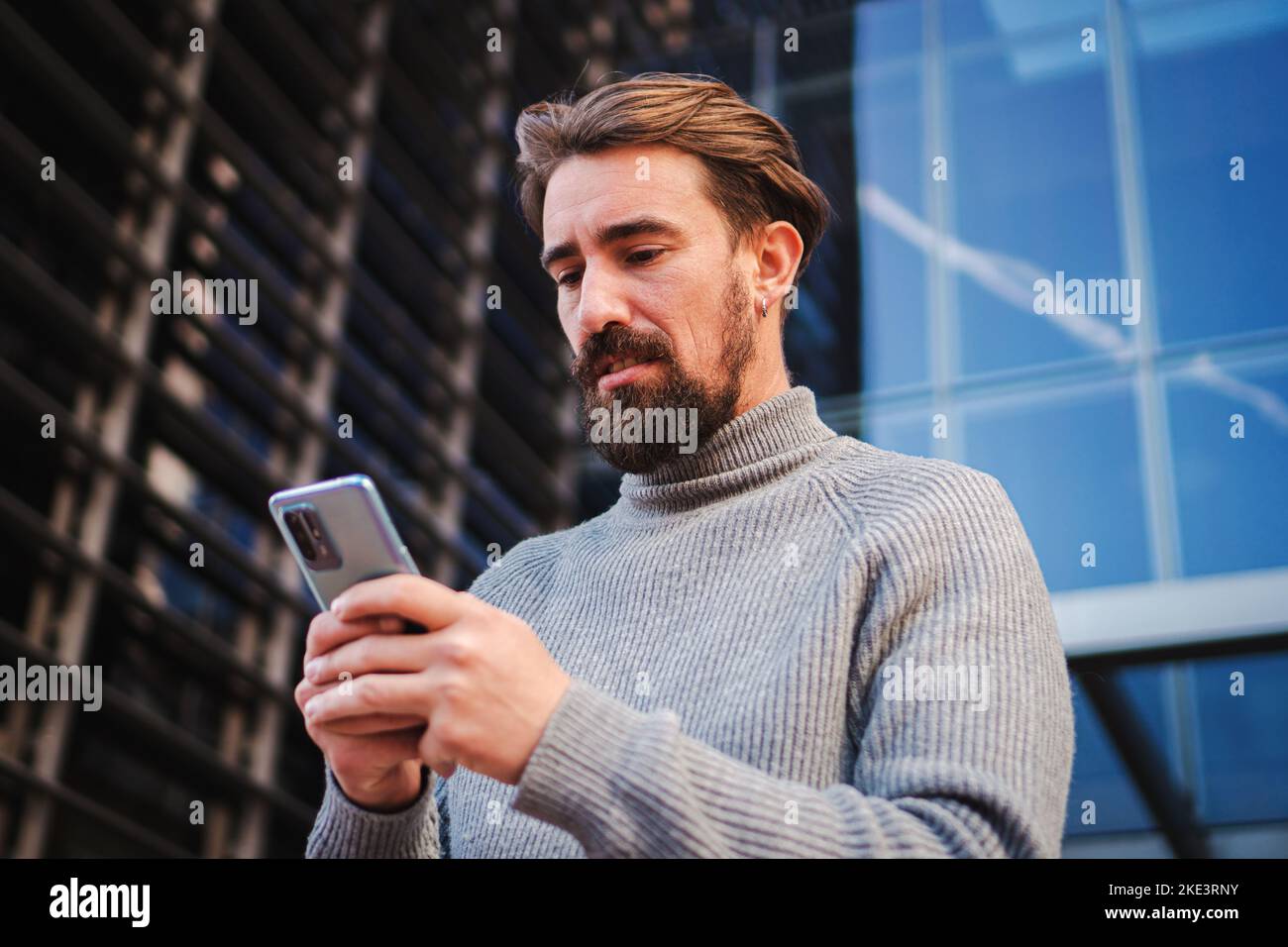 Un giovane serio si è concentrato e preoccupato di utilizzare un'app per telefono cellulare per inviare SMS e condividere contenuti multimediali su un'area di lavoro Foto Stock