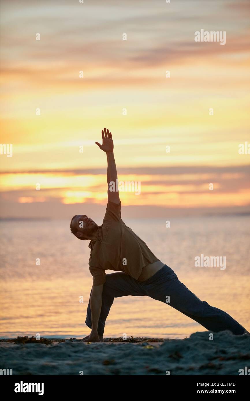 Yoga - leghi il corpo e la mente. Un uomo che pratica il triangolo posa durante la sua procedura di yoga alla spiaggia. Foto Stock