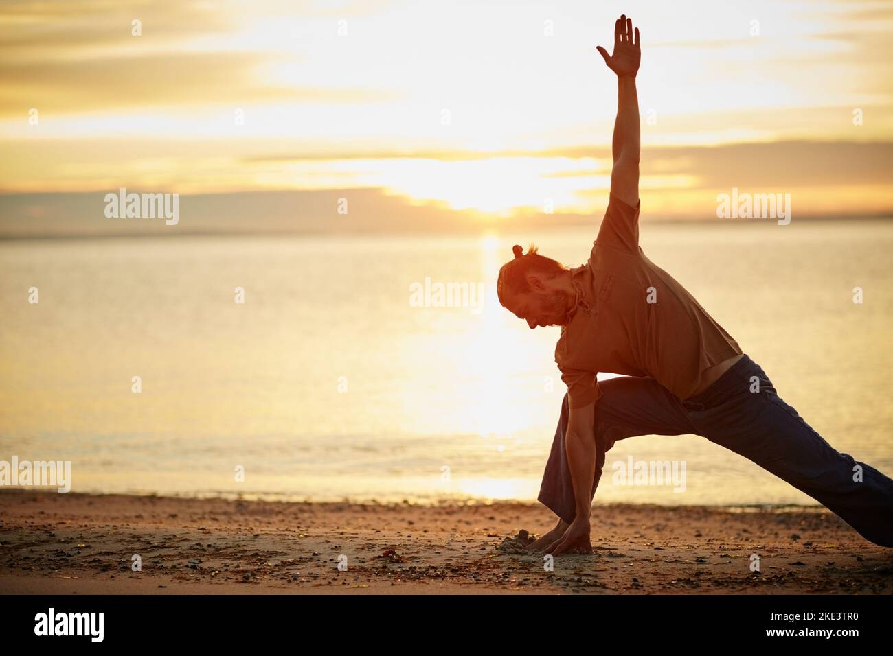 Sfida il corpo, calma la mente. Un uomo che pratica il triangolo posa durante la sua routine di yoga in spiaggia. Foto Stock