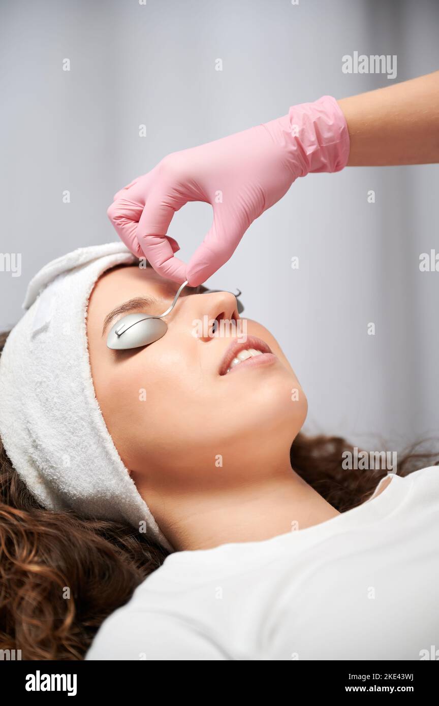 Primo piano faccia di giovane donna in corso di procedura medica. Una mano in guanto rosa che mette la protezione dell'occhio del metallo dalla luce laser sul paziente prima del resurfacing del laser per ringiovanimento facciale. Foto Stock