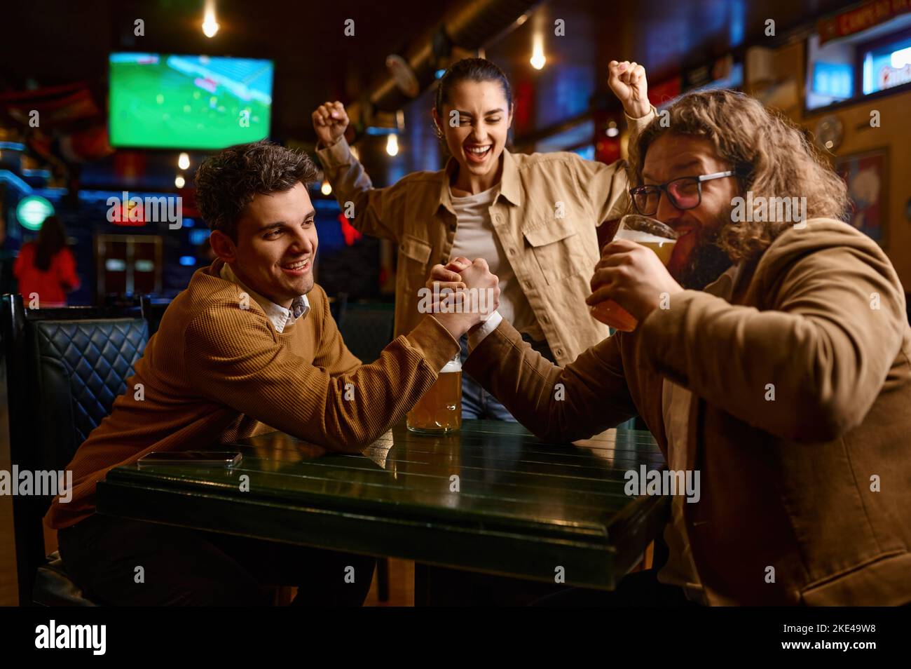 Amici felici che si divertono a fare il wrestling delle braccia allo sport bar Foto Stock