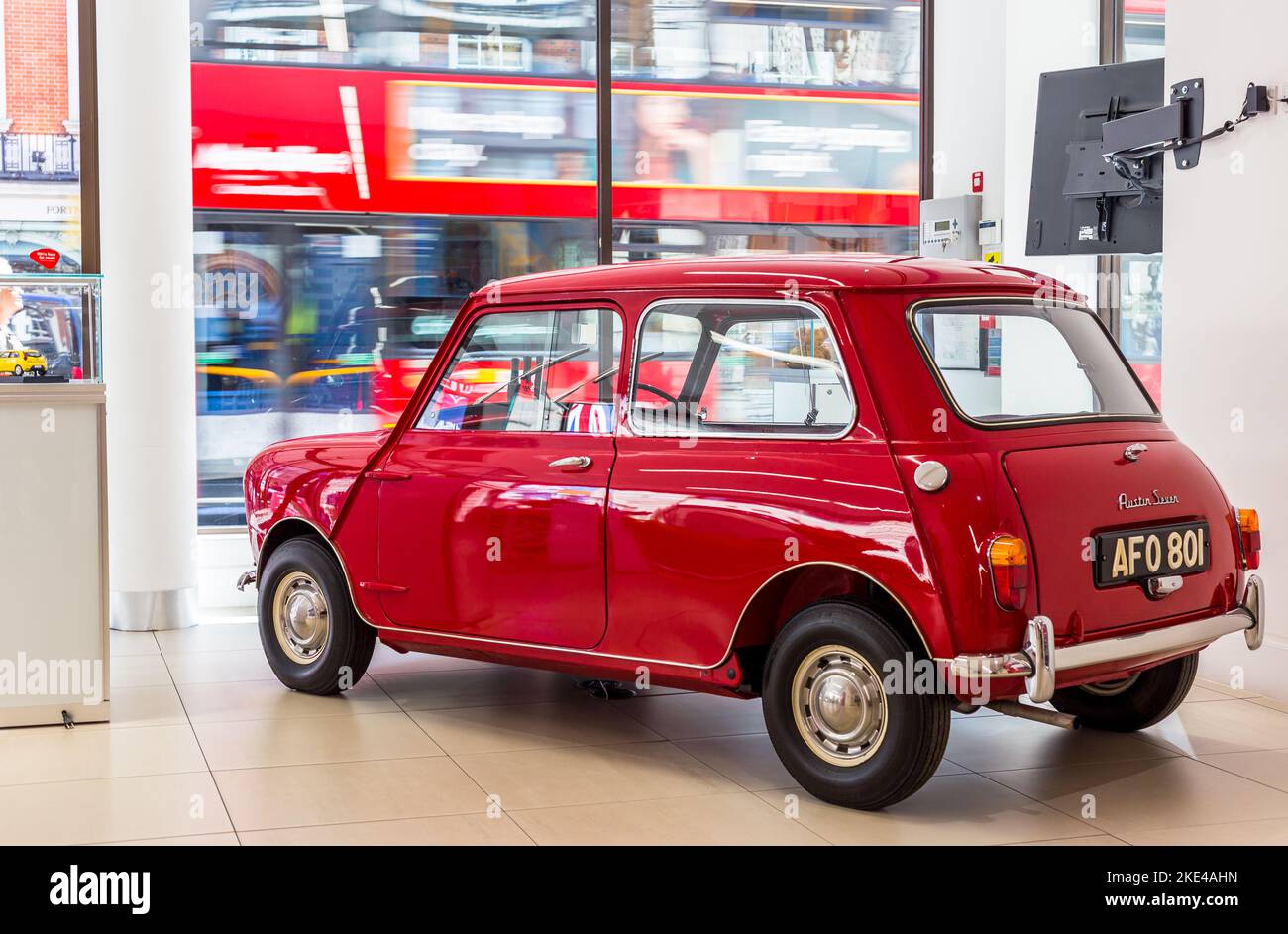 Un mini Austin originale splendidamente restaurato è parcheggiato in uno showroom nell'estremità ovest. Il mini è parcheggiato da una grande finestra mentre un autobus rosso passa accanto Foto Stock