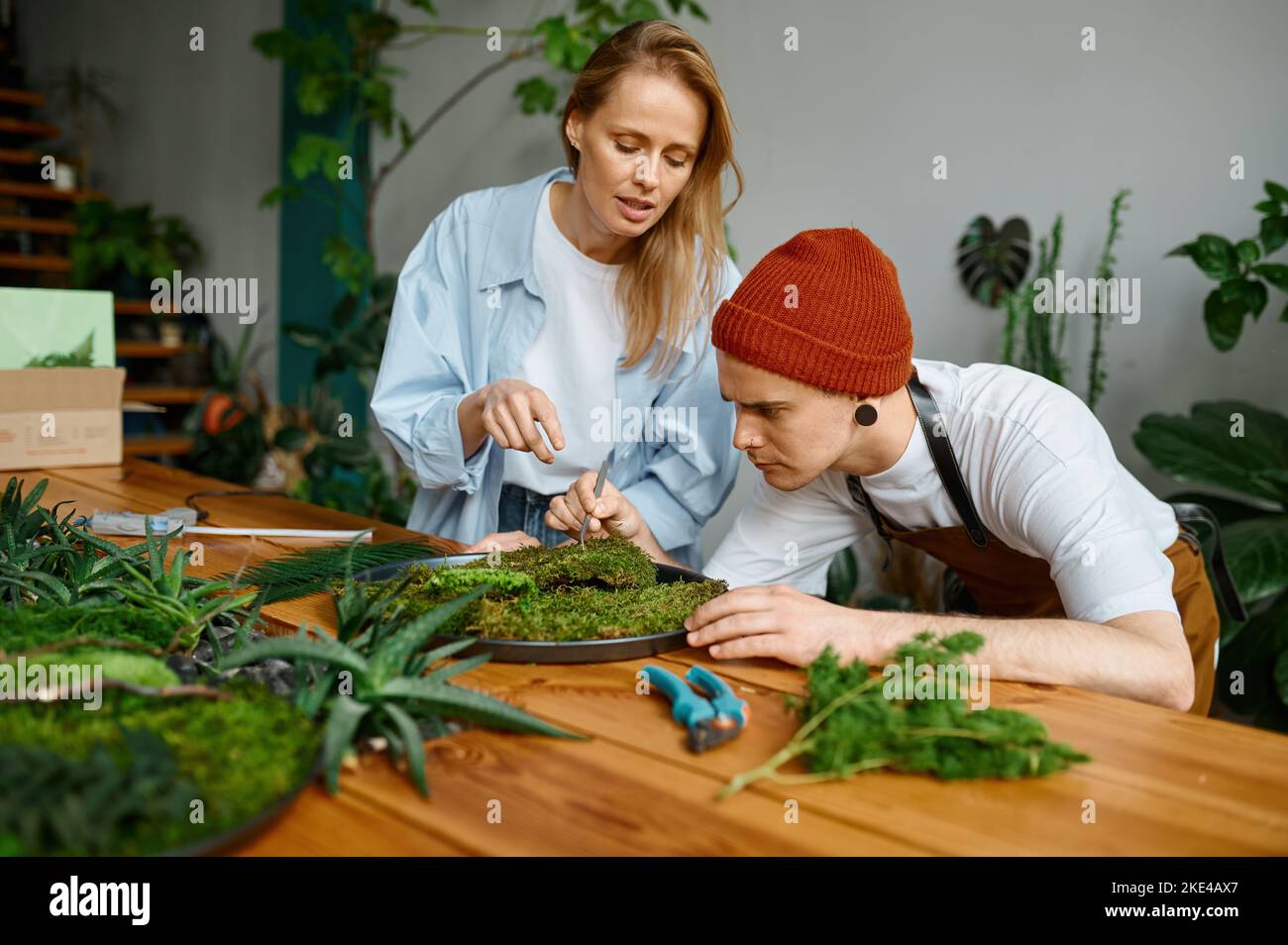 Fiorista donna che insegna giovane uomo hipster decoratore a studio arte artigianale Foto Stock