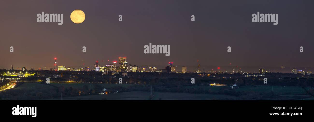Panoramica, vista notturna da una distanza di luna piena che sorge sul centro di Birmingham, Regno Unito. Foto Stock