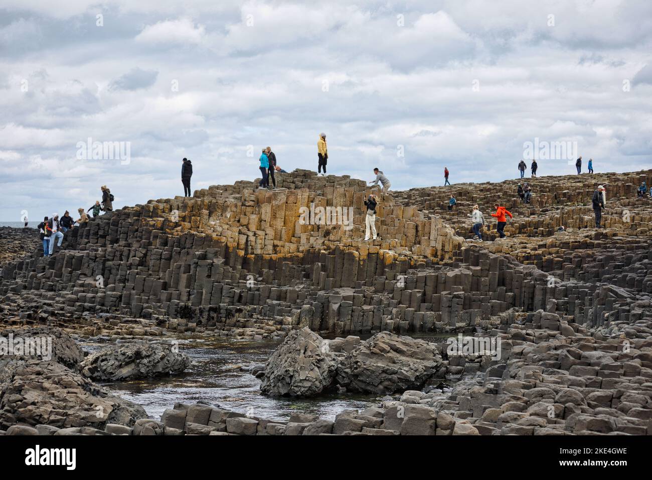 I turisti che si arrampicano sulle antiche colonne basaltiche del Selciato del gigante, patrimonio dell'umanità dell'UNESCO, Causeway Coast, County Antrim, Irlanda del Nord Foto Stock