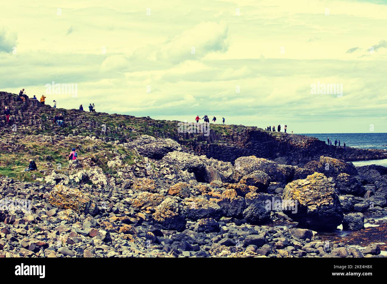 I turisti che si arrampicano sulle antiche colonne basaltiche del Selciato del gigante, patrimonio dell'umanità dell'UNESCO, Causeway Coast, County Antrim, Irlanda del Nord Foto Stock