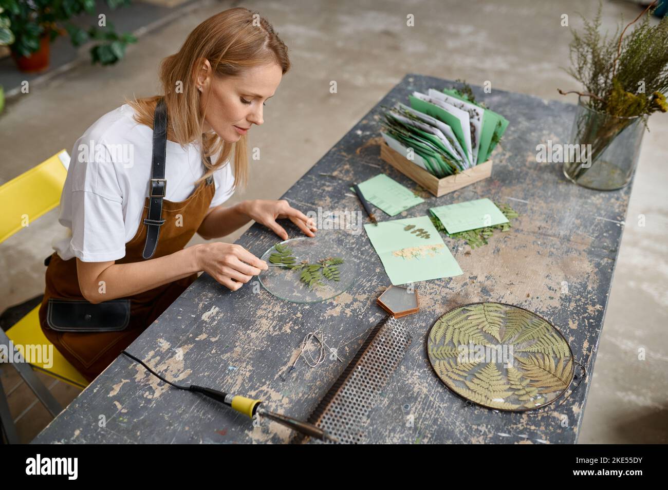 Un'artista femminile che fa una composizione floreale creativa nello spazio di lavoro Foto Stock