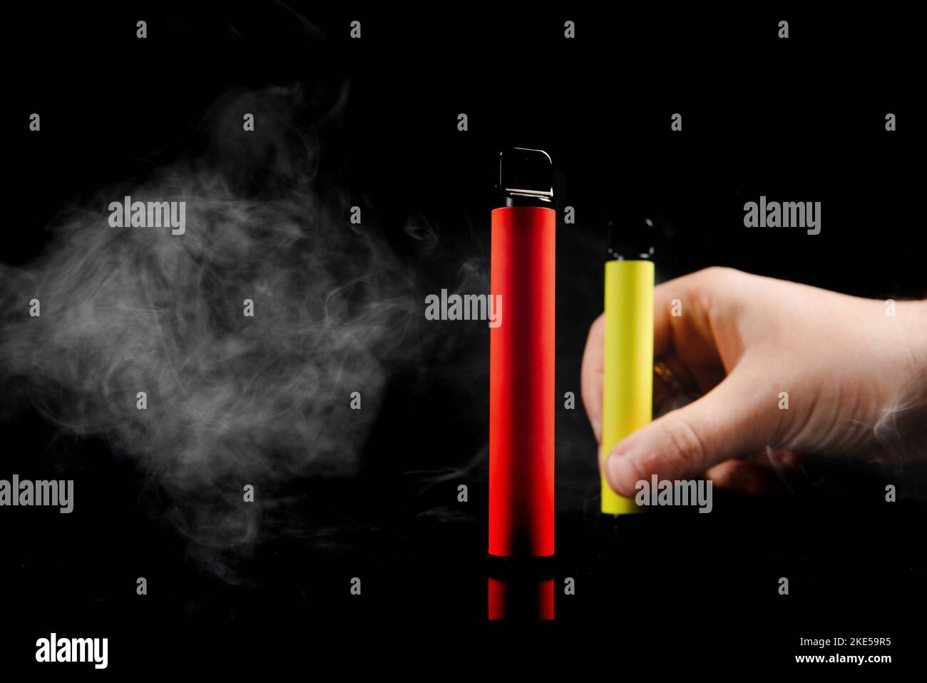 Sigarette elettroniche usa e getta di diversi gusti in mano su sfondo giallo. Il concetto di fumo moderno, vaping e nicotina. Foto Stock