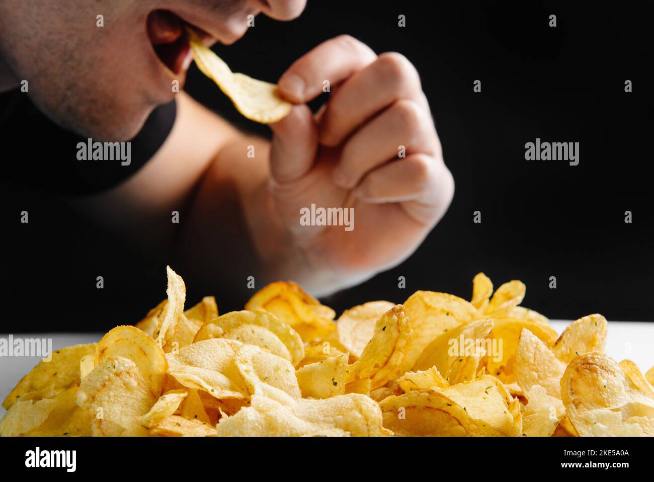 L'uomo sta mangiando cibo spazzatura, patatine su uno sfondo scuro. Cibo nocivo. Il cibo fritto è dannoso per la salute. Stile di vita sano, alimentazione corretta, divieto Foto Stock