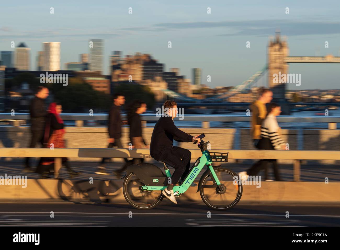 Un uomo che si trova in viaggio su una bicicletta elettrica a noleggio attraverso il London Bridge, durante l'ora di punta. London Bridge, Londra, Regno Unito. 28 Ott 2022 Foto Stock