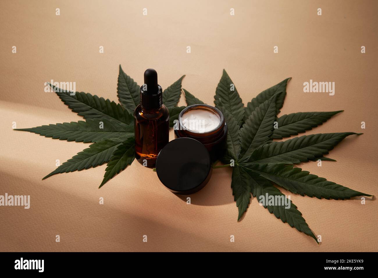 Un mock-up per il viso e il corpo prodotto cosmetico a base di cannabis medica. Siero o olio e crema su sfondo marrone chiaro. Copia spazio . Concetto di salute e benessere. Foto Stock