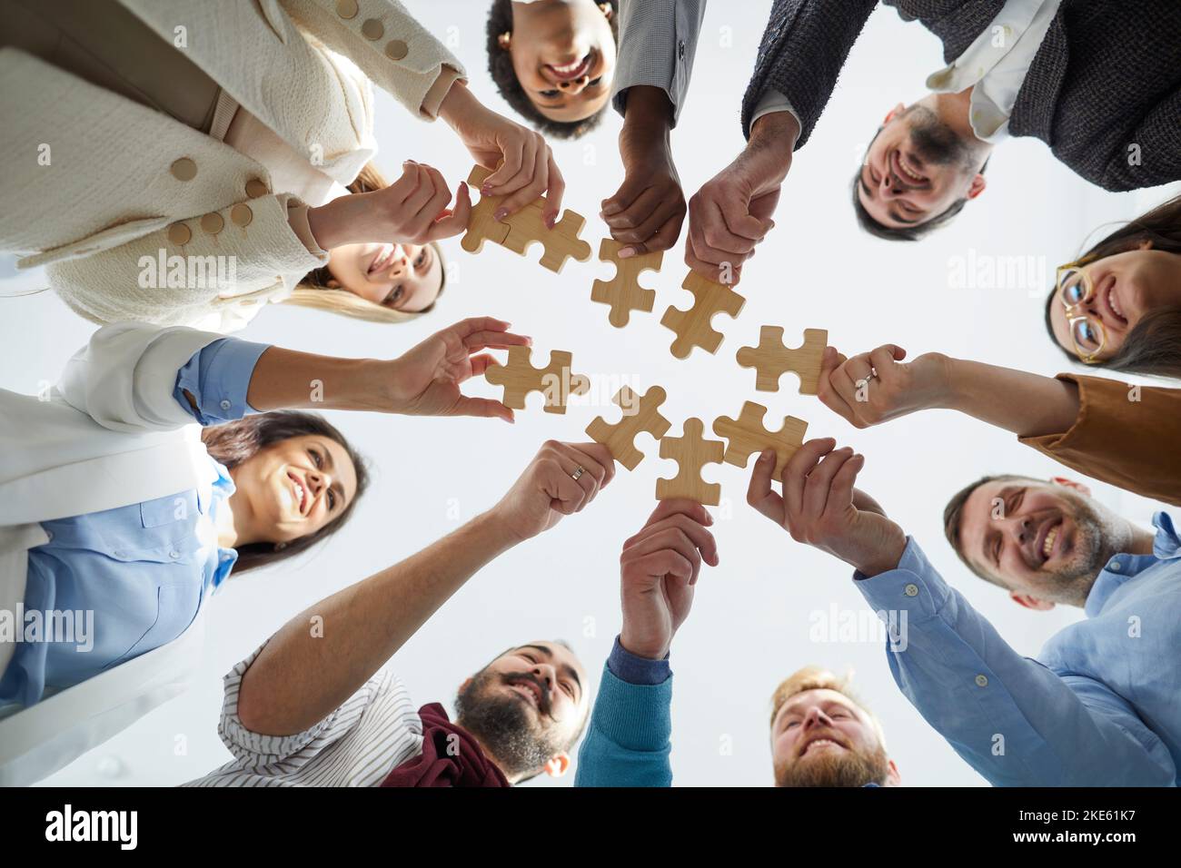 Pezzi di legno di puzzle nelle mani di gente allegra e gioiosa di affari che li collegano. Foto Stock