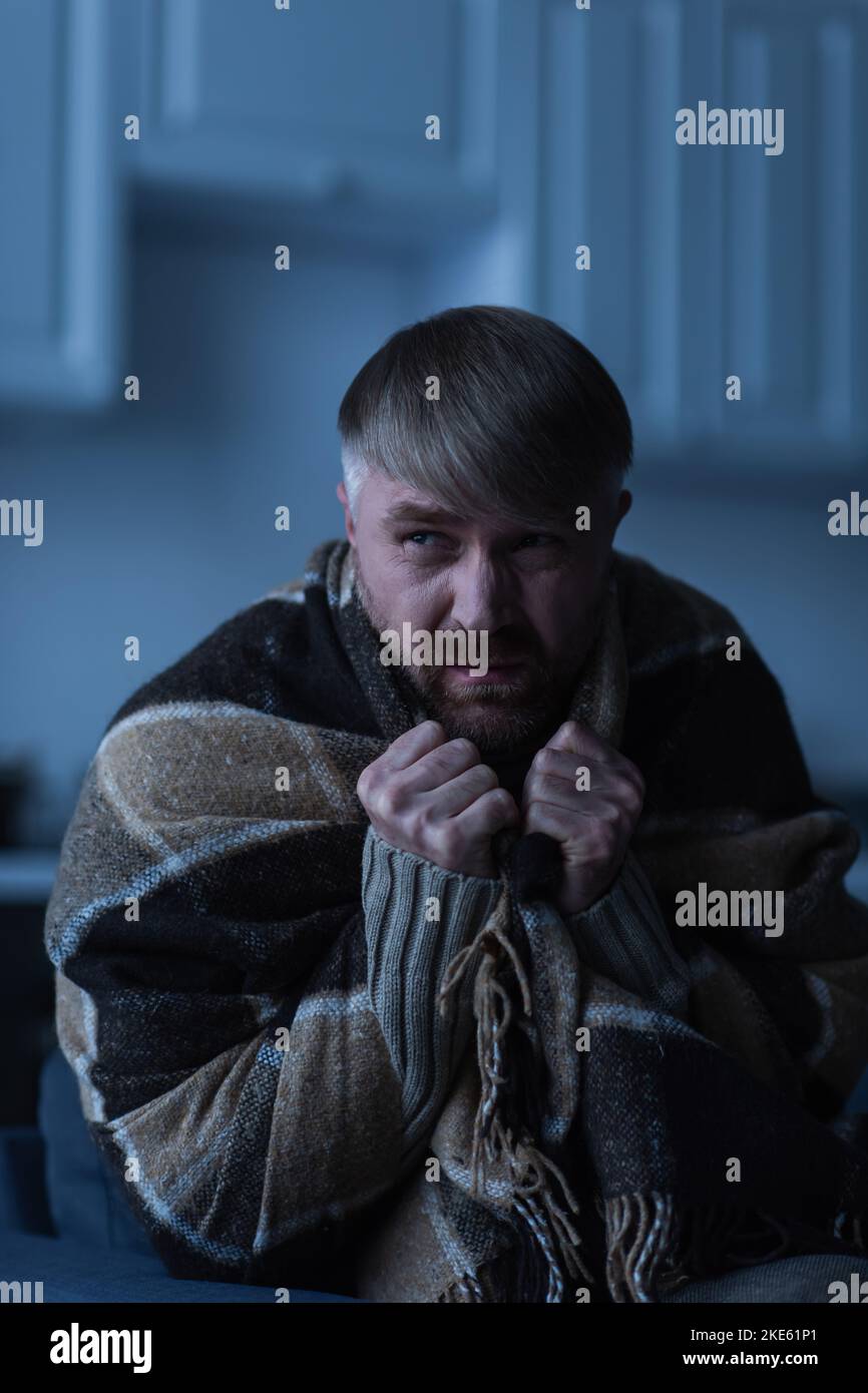 uomo dispiaciuto avvolto in una calda coperta e guardato via durante il blackout Foto Stock