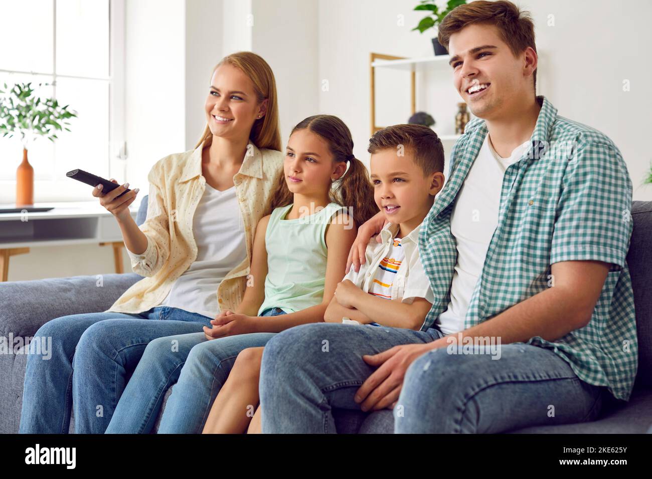 La famiglia giovane e allegra con i bambini si rilassa guardando i programmi televisivi insieme. Foto Stock