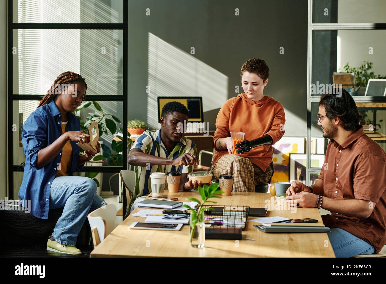 Gruppo di giovani colleghi interculturali che hanno snack e caffè a pranzo nel bel mezzo della giornata lavorativa sul posto di lavoro in ufficio Foto Stock
