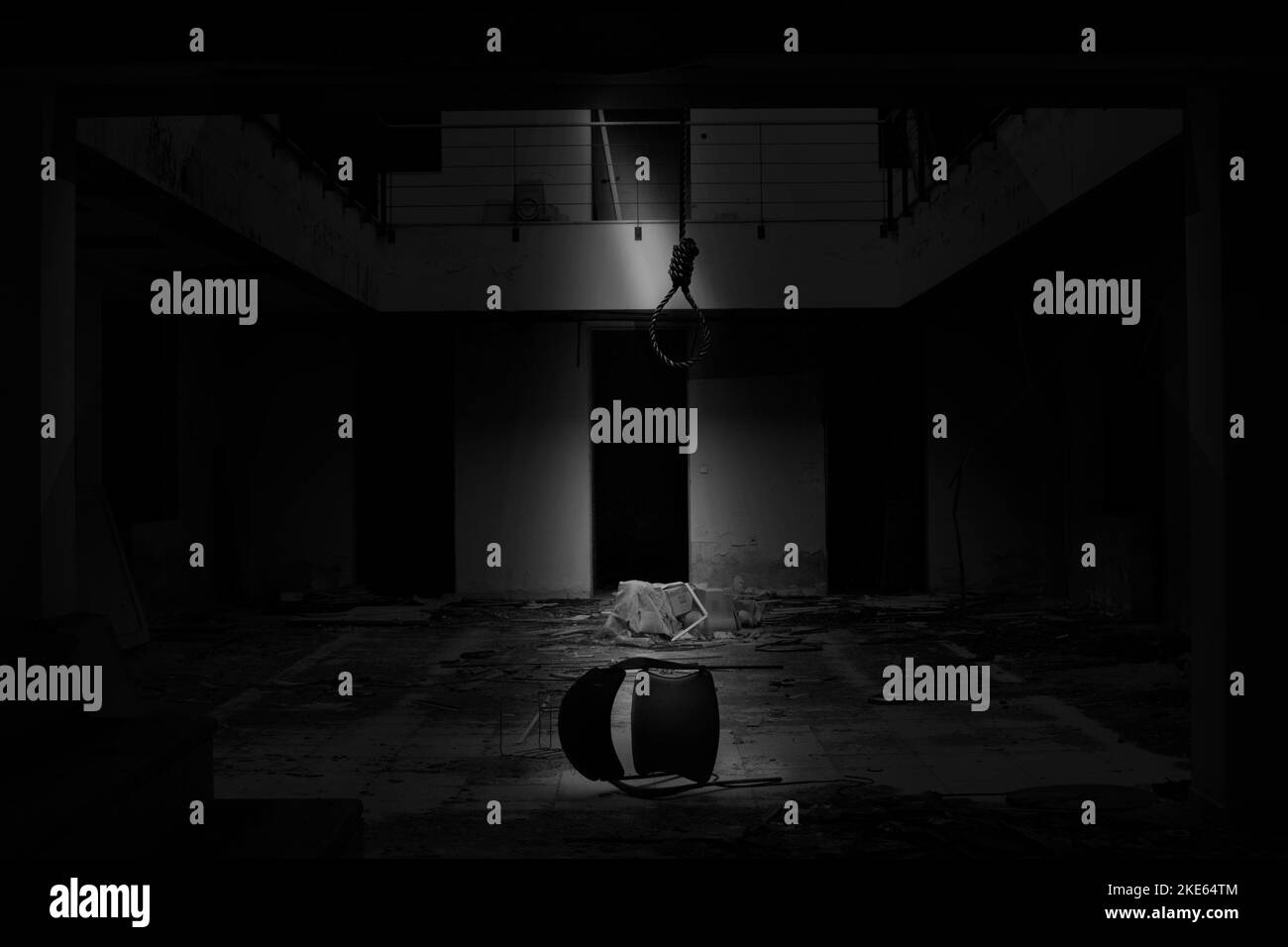 Un'immagine monocromatica di un edificio abbandonato con una sedia sul pavimento e un anello di corda sospeso da un soffitto, un concetto di suicidio Foto Stock