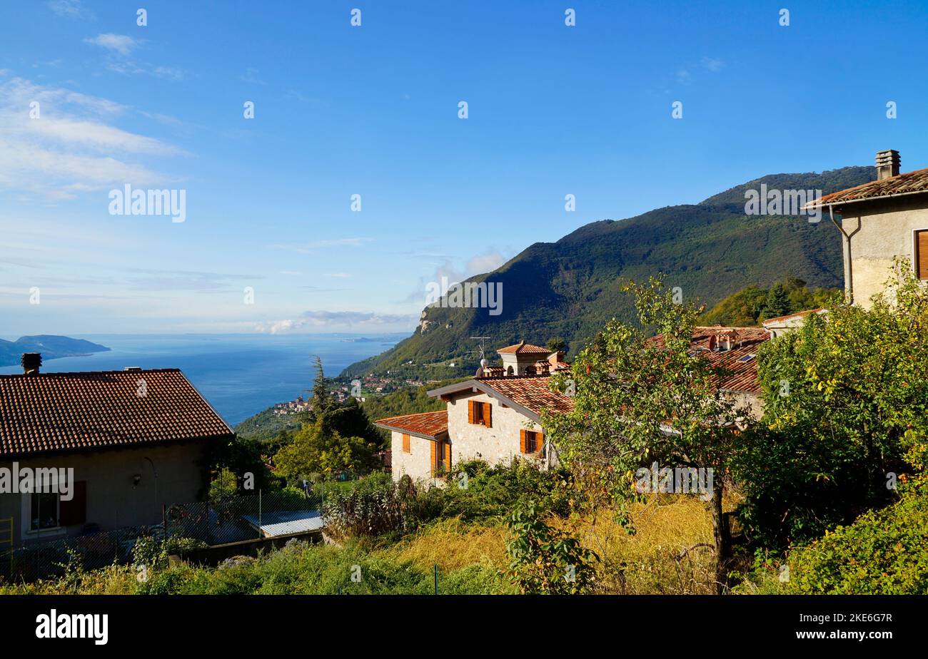 Scenario mediterraneo soleggiato con un villaggio italiano che domina il vasto lago di Garda e le Alpi italiane vicino a Tignale, Lombardia, Italia Foto Stock