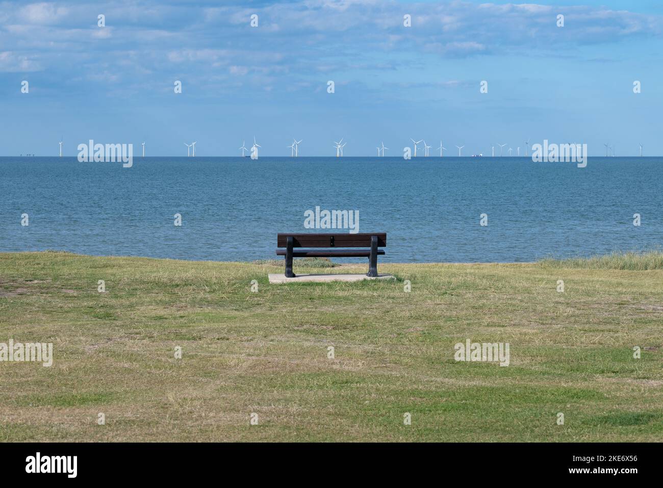Panchina sul lungomare di Leysdown, con vista sulla centrale eolica all'aperto di Kentish Flats, Isola di Sheppey, Kent, Inghilterra, Regno Unito Foto Stock