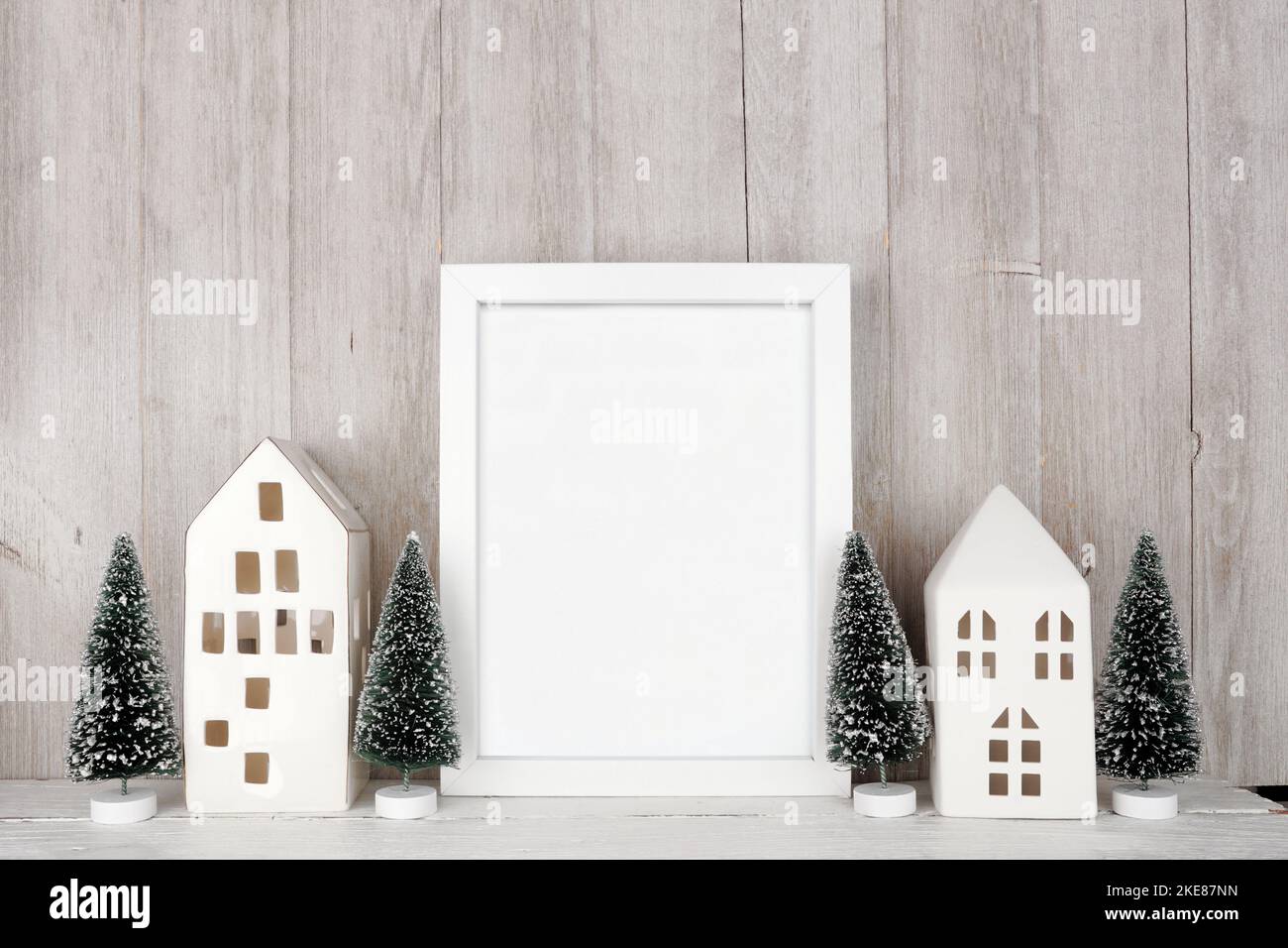 Natale mock up con cornice bianca, case bianche e decorazione ad albero. Cornice verticale su una mensola di legno contro uno sfondo rustico grigio pannello parete. Copia Foto Stock