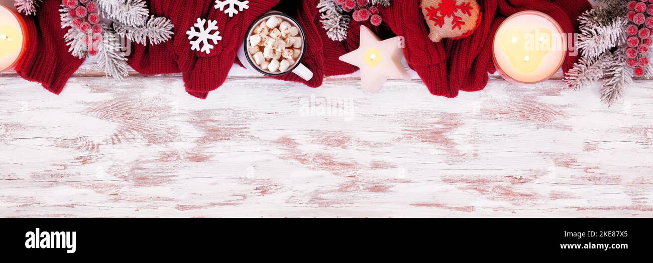 Accogliente bordo superiore di Natale o inverno con maglione rosso, candele, cioccolata calda, rami gelosi e decorazioni. Sopra vista su un rustico banner in legno bianco ba Foto Stock
