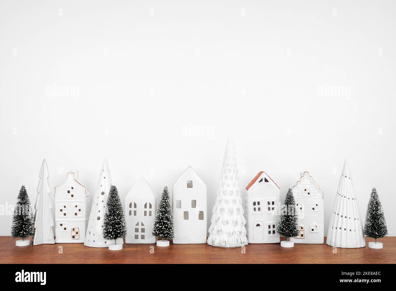 Decorazioni bianche natalizie su una mensola di legno contro uno sfondo bianco parete con spazio copia. Alberi e case di villaggio. Foto Stock