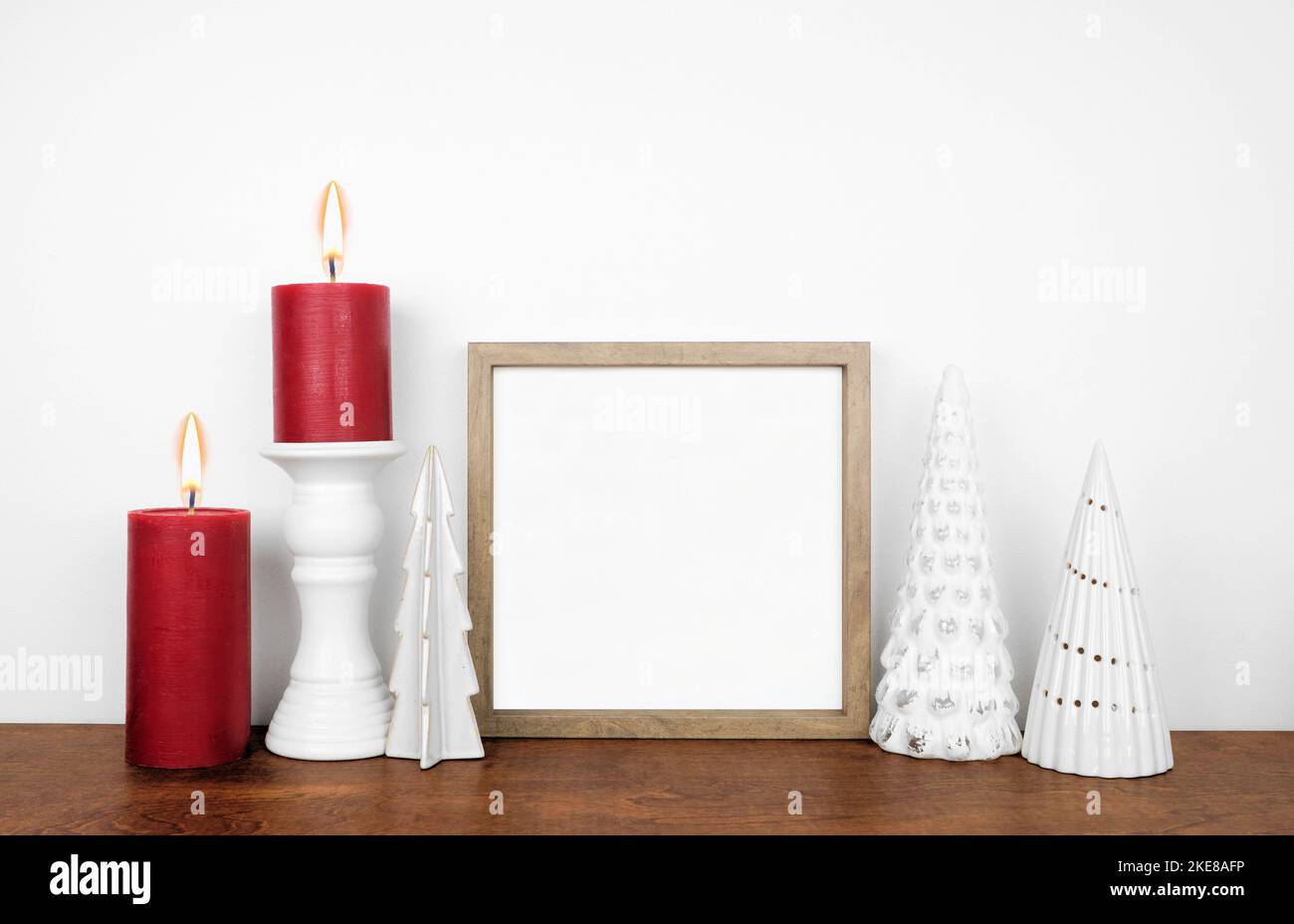 Natale mock up con cornice in legno, albero bianco decorazione e candele rosse. Cornice quadrata su una mensola di legno contro una parete bianca. Spazio di copia. Foto Stock
