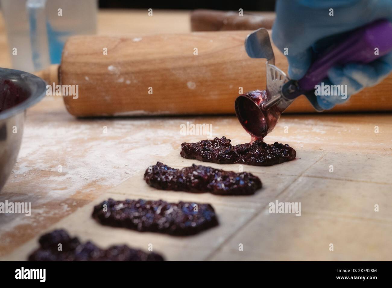 Un panettiere sfoglia il ripieno di frutti di bosco sull'impasto con un mattarello sullo sfondo Foto Stock