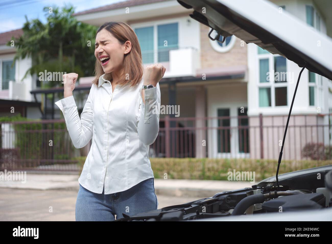 Giovane donna sconvolta in piedi vicino alla macchina rotta con il cofano aperto. Foto Stock