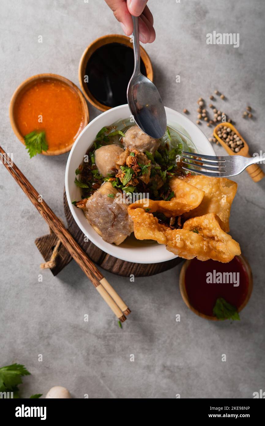 Bakso o polpetta indonesiana servita con zuppa di brodo, tofu, noodle e wonton fritto o gnocchi su un recipiente bianco Foto Stock