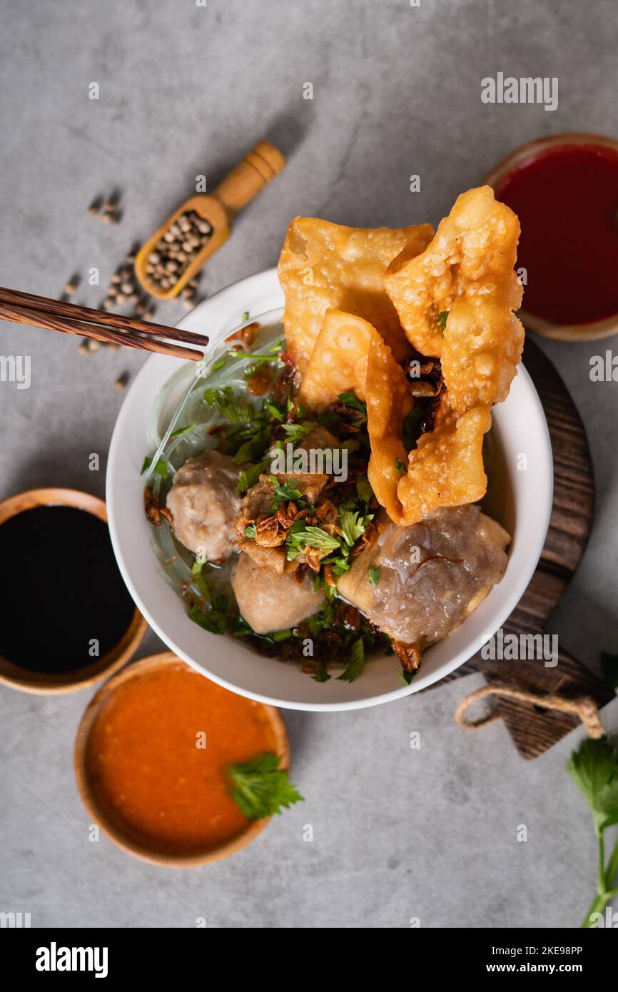 Bakso o polpetta indonesiana servita con zuppa di brodo, tofu, noodle e wonton fritto o gnocchi su un recipiente bianco Foto Stock