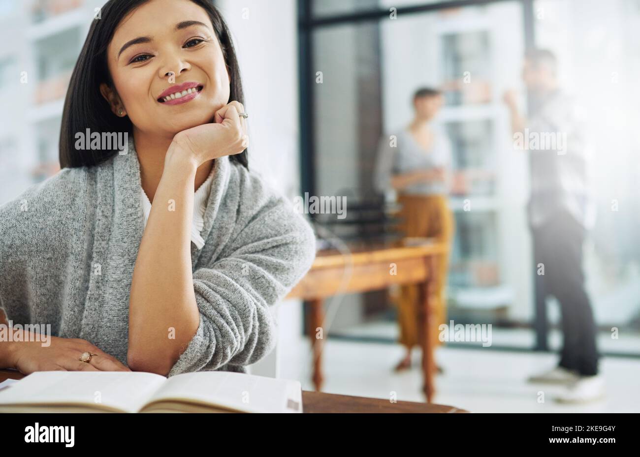 Avete bisogno di fiducia se volete un colpo al successo. Ritratto di una giovane donna d'affari seduta alla sua scrivania con i colleghi sullo sfondo. Foto Stock