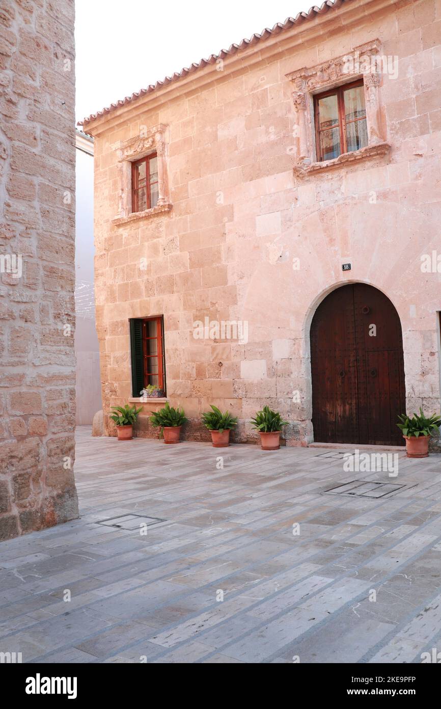 Antico muro di pietra con porta in legno e fiori vaso in una strada nel centro storico di Alcudia, Maiorca, Spagna. Foto Stock