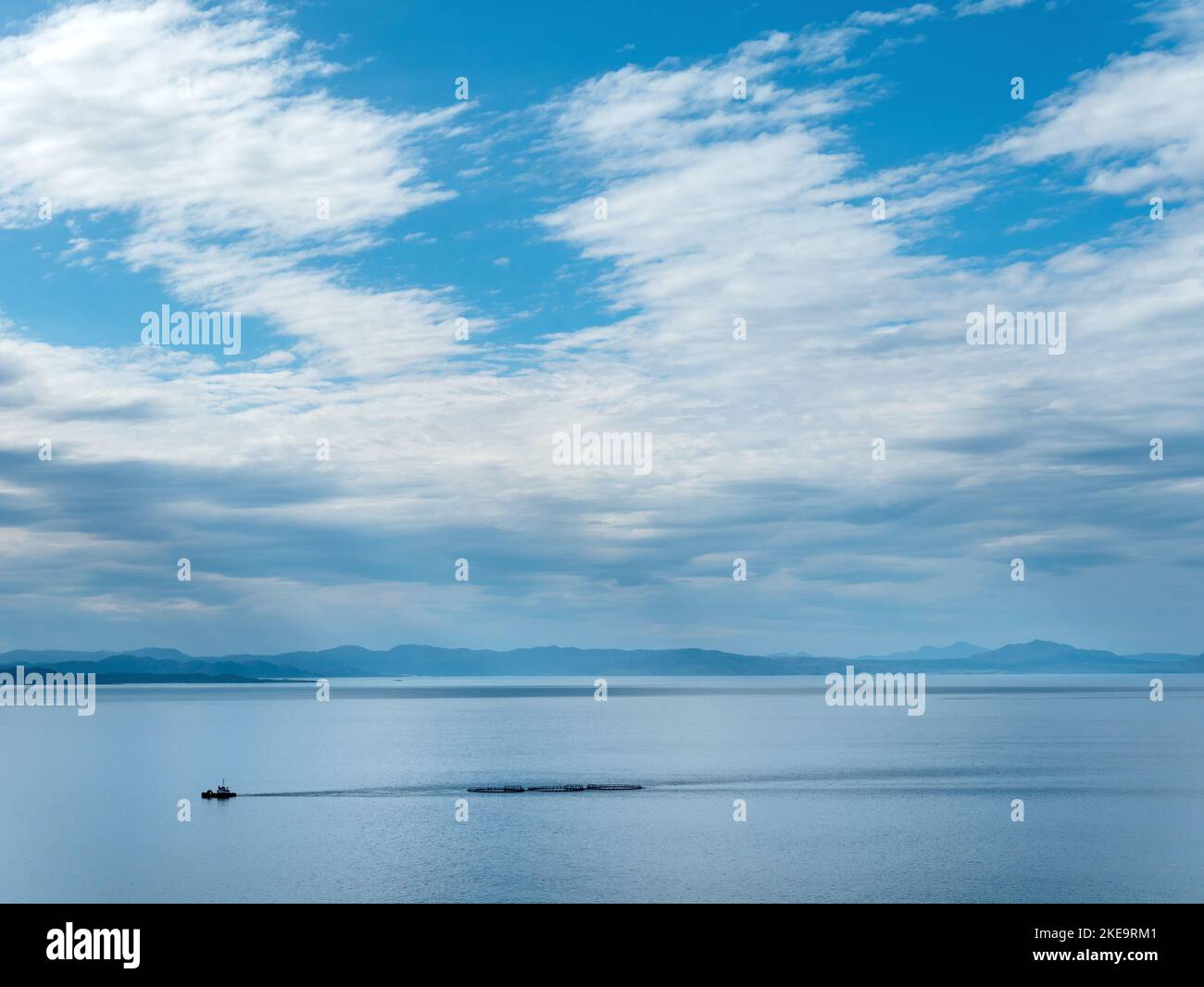 Piccola barca che traina gabbie di fattoria di pesce lungo il Sound of Sleat, Isola di Skye, Scozia, Regno Unito Foto Stock