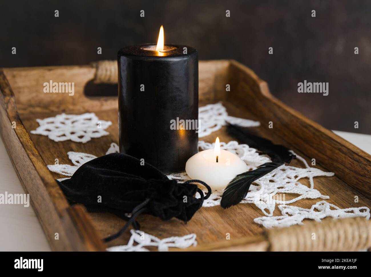 Nero e bianco candele bruciare, colore nero velluto coulisse borsa regalo, bianco fiocchi di neve uncinetto fatto a mano su vassoio di legno di colore naturale in casa, al coperto Foto Stock