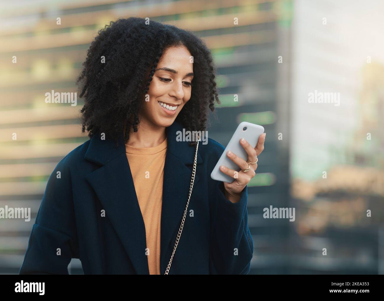 Telefono, social media e comunicazione con una donna di colore aziendale che digita un messaggio di testo in città. Mobile, networking e contatto con un felice Foto Stock