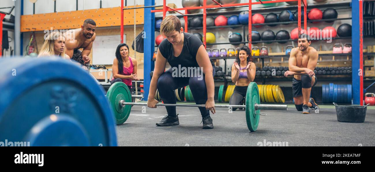 Donna pronta a fare il sollevamento pesi mentre i suoi compagni di palestra che la incoraggiano Foto Stock