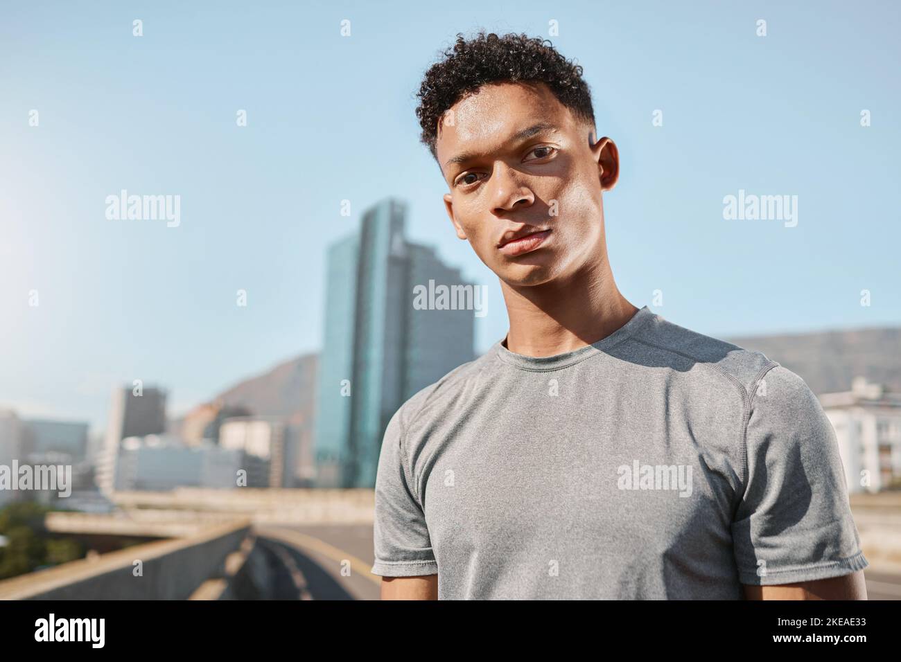 Giovane uomo nero e ritratto sul ponte con edifici, cielo e città per correre. Uomo, fitness e allenamento in città, metropolitana o città sotto il sole estivo Foto Stock