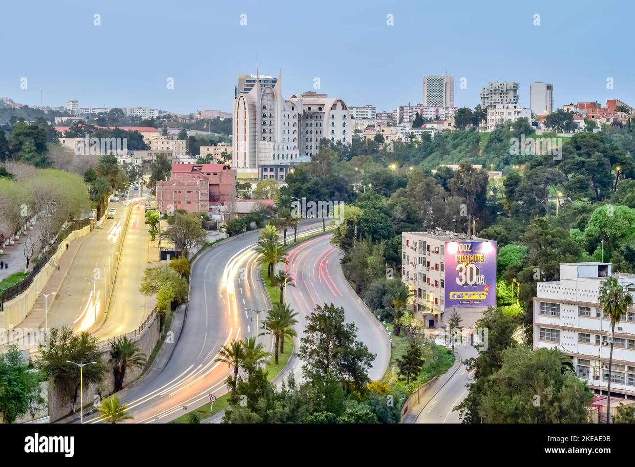 L'hotel Golden Palace è in costruzione e la torre AGB sull'autostrada Benaknoun. Una vista aerea a lunga esposizione con le luci delle auto in movimento, gli alberi e il cielo blu. Foto Stock