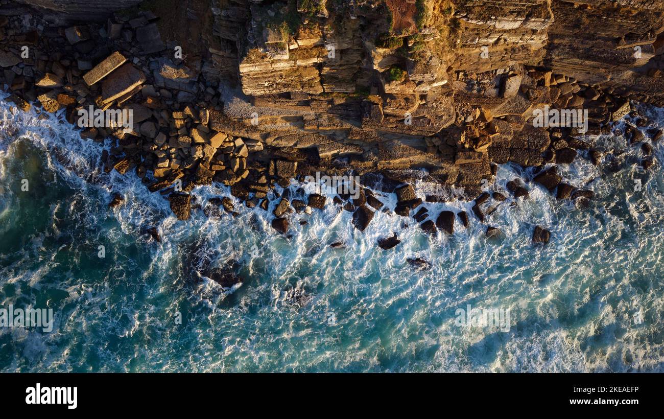 Vista aerea delle onde dell'oceano che si infrangono contro le rocce di una scogliera durante il tramonto. Viaggi e vacanze. Momenti di relax. Foto Stock