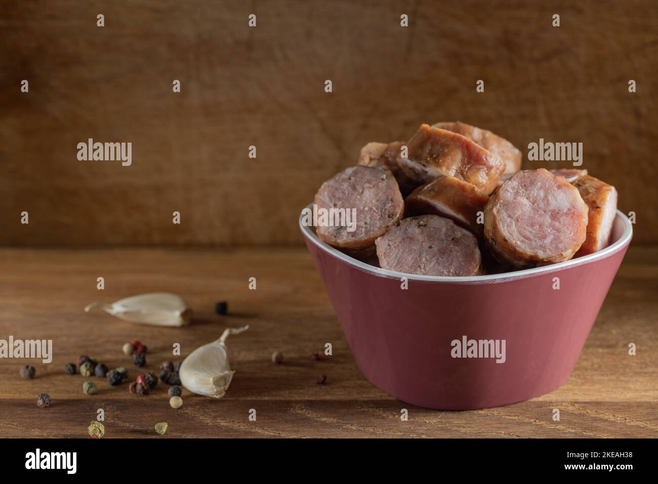 Fette di salsicce di maiale affumicate in ciotola con spezie su fondo di legno Foto Stock
